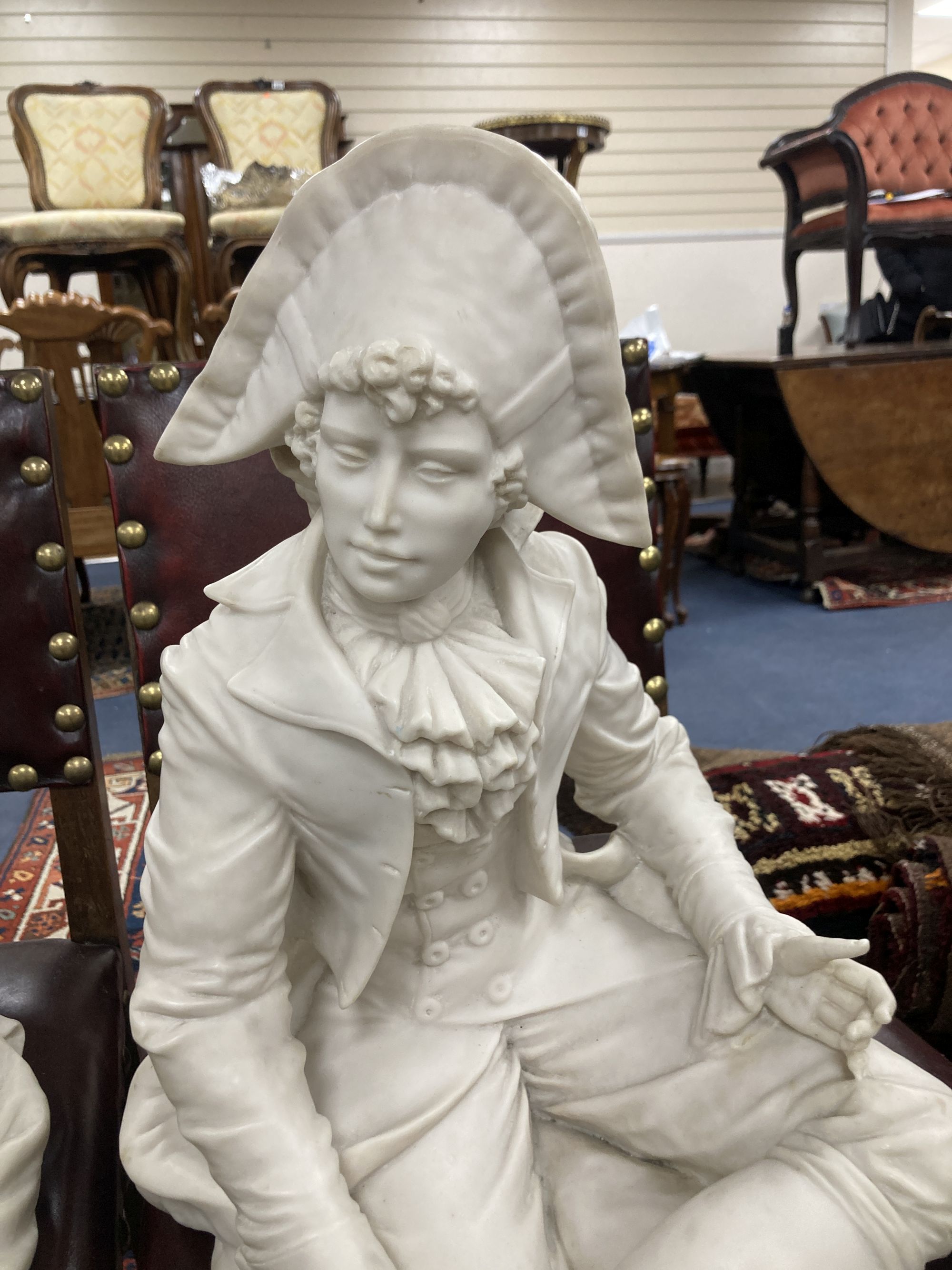 A pair of resin marble seated figures of a Dandy and a Dandizette on ebonised plinths